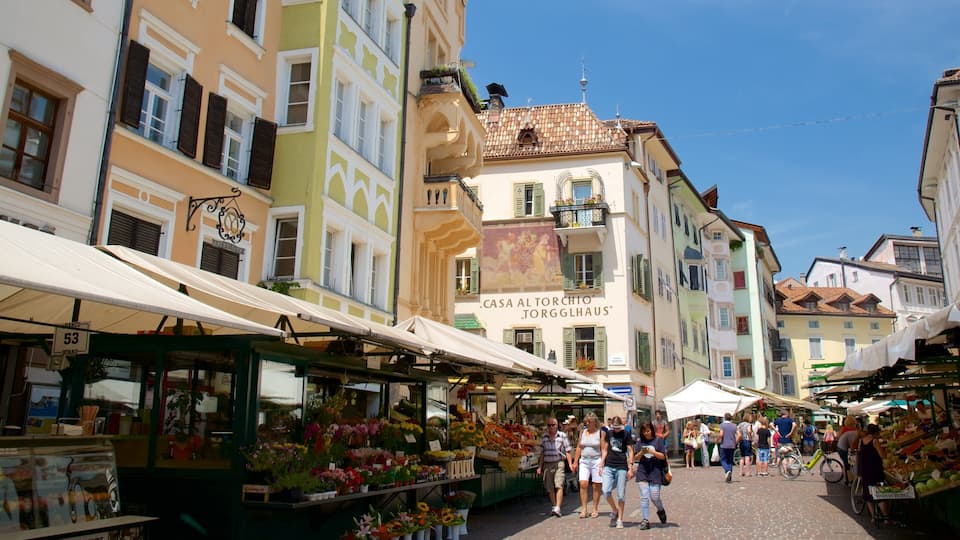A bustling outdoor market with colorful buildings and vendors selling flowers and fruits.