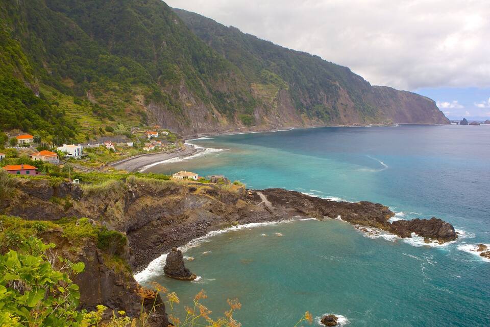 A coastal village with houses on a hillside overlooking turquoise waters and rocky cliffs.