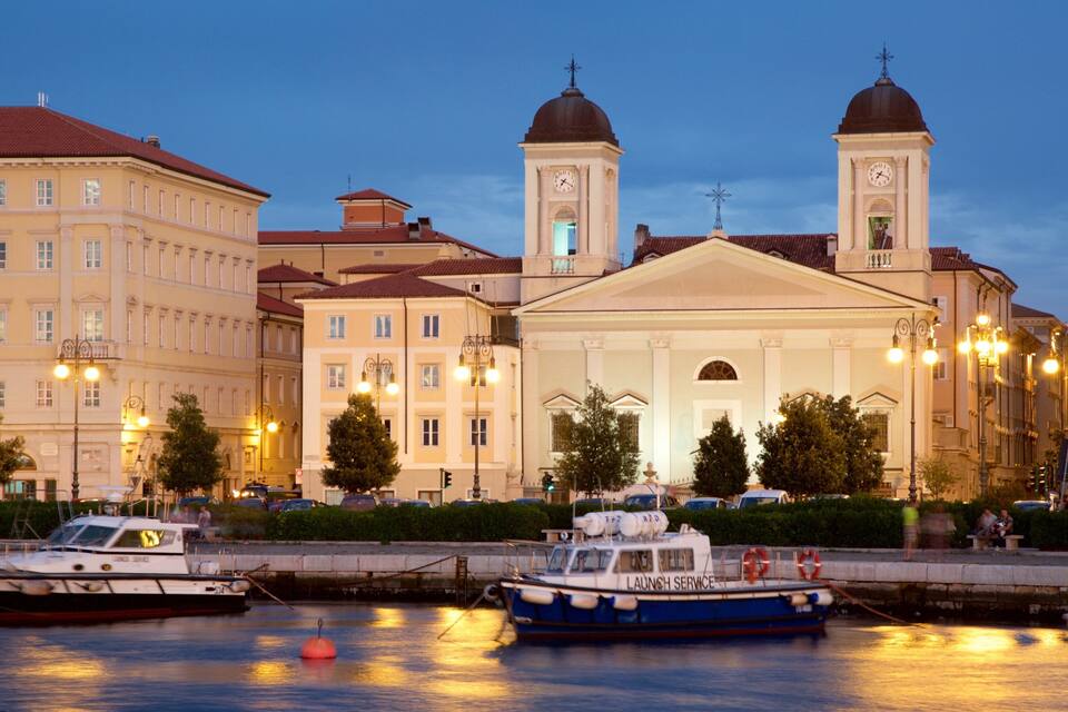 A waterfront with boats, a church with two towers, and classical architecture.