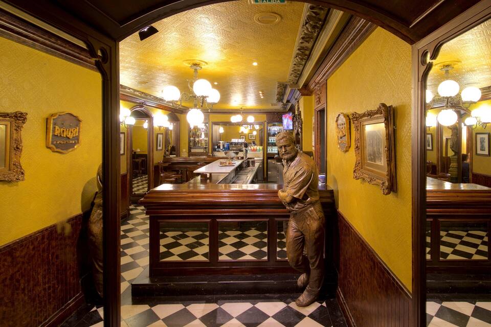 A restaurant interior with a checkered floor, wooden benches, and a statue of a man.