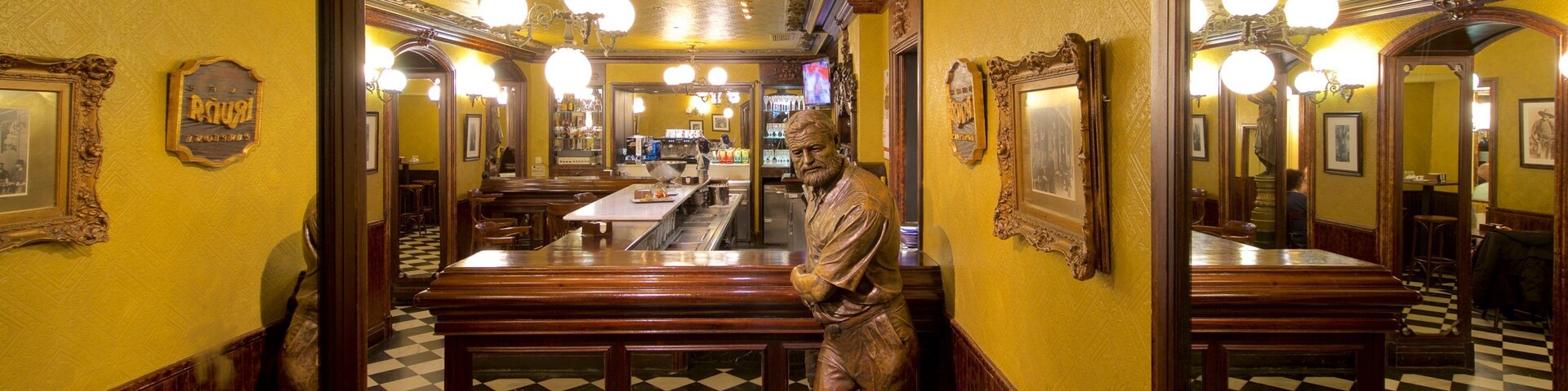 Interior de restaurante con suelo a cuadros, bancos de madera y una estatua de un hombre.