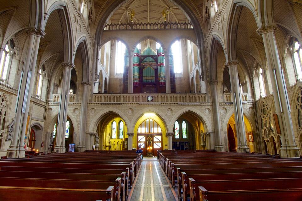A grand cathedral interior with high vaulted ceilings, stained glass windows, and rows of wooden pews.