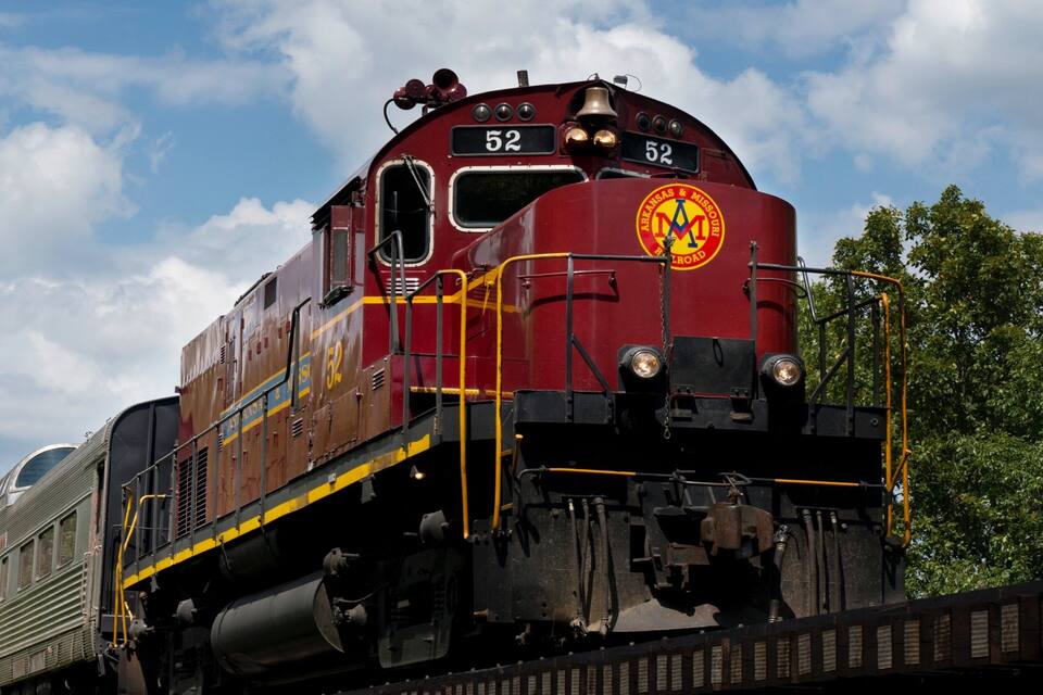 A red train with the number 52 on it, moving on tracks with trees in the background.