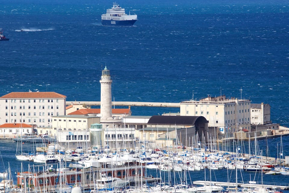 A harbor with numerous boats, a lighthouse, and a large building with a red roof.