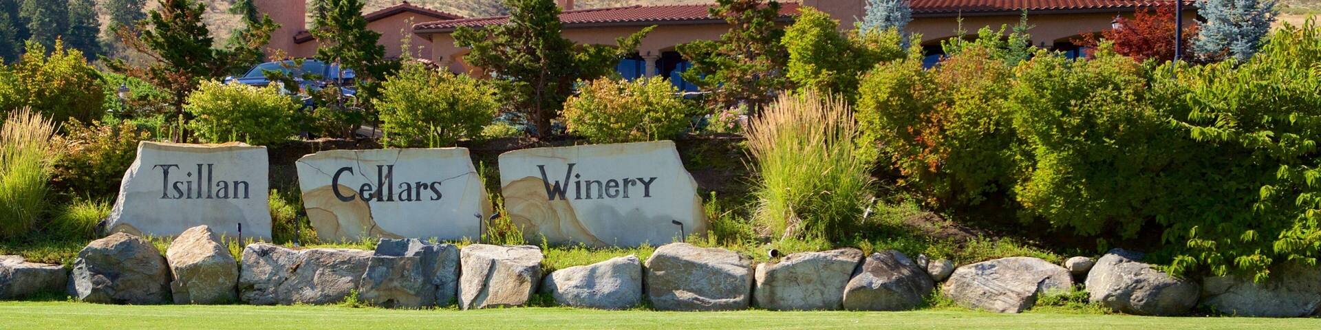 A winery with a clock tower, surrounded by a well-maintained lawn and a mountainous backdrop.