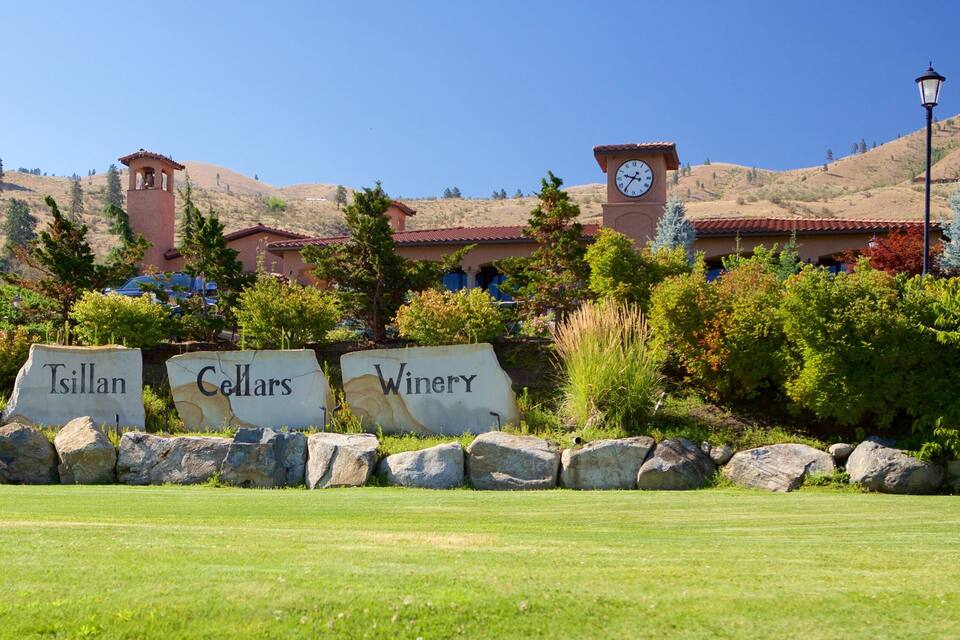 A winery with a clock tower, surrounded by a well-maintained lawn and a mountainous backdrop.
