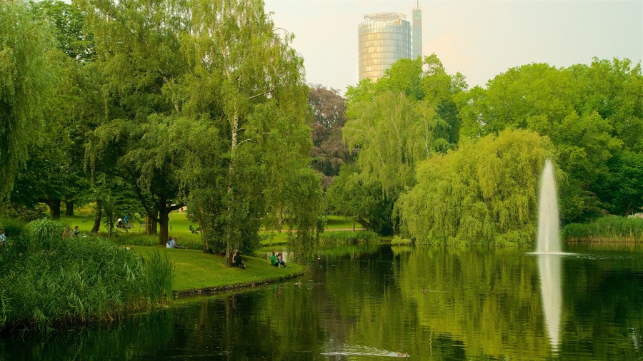 A park with a pond, trees, and a fountain.