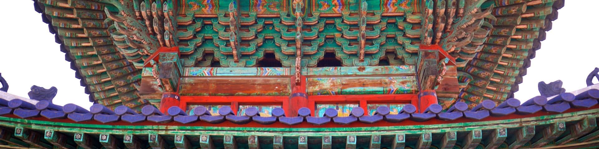 Un edificio tradicional chino con tejas ornamentales verdes y rojas, elaborados adornos de madera y una base de ladrillo.