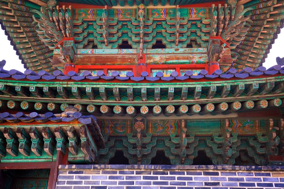 Un bâtiment traditionnel chinois, caractérisé par ses tuiles vertes et rouges richement décorées, ses sculptures complexes en bois et sa base en briques.