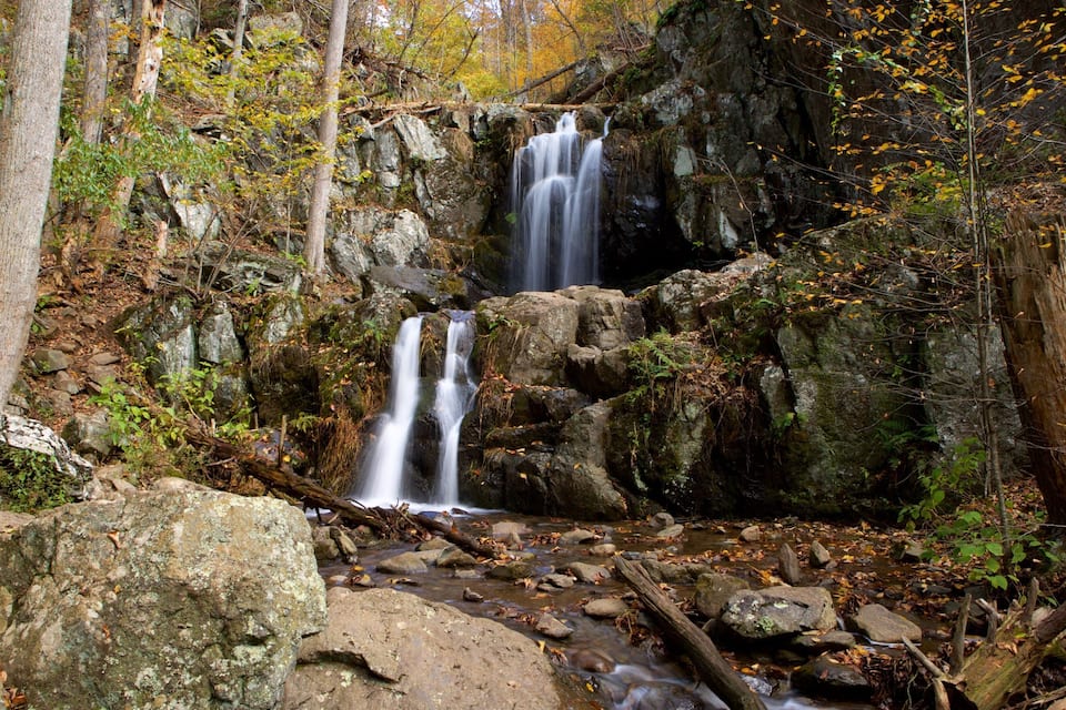 Una cascada en una zona boscosa amb roques i fulles d'automne.