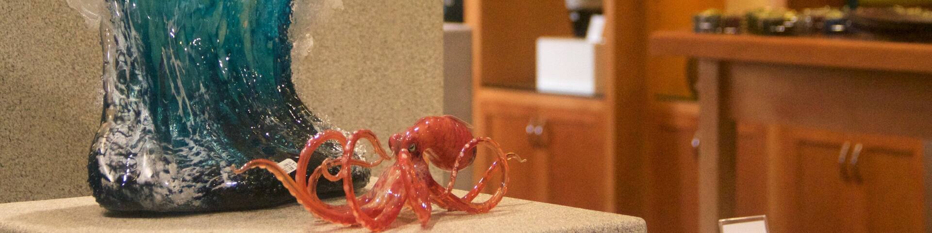 Una escultura de vidrio de una ola con un pulpo rojo a su lado.