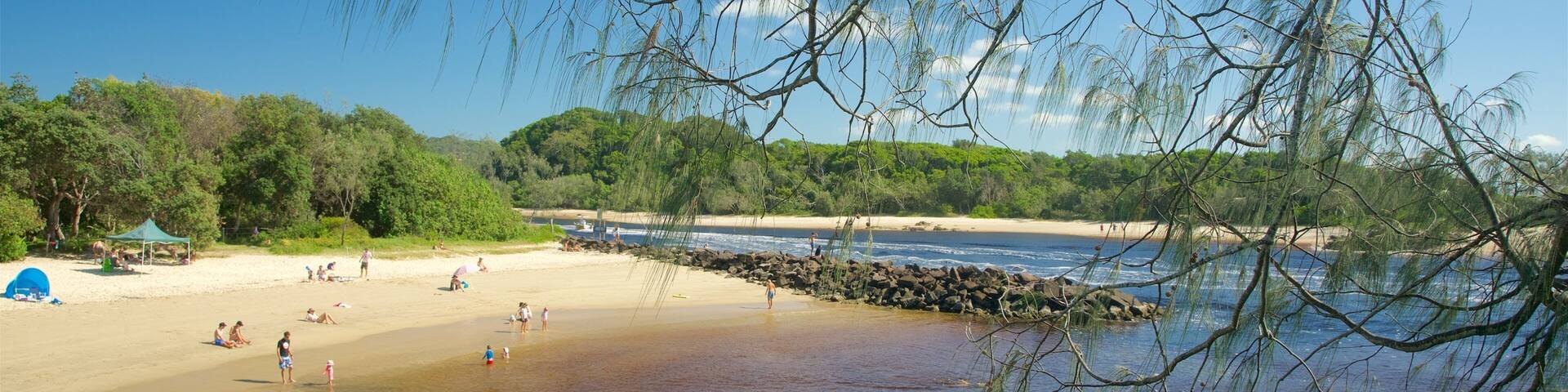 Una playa con agua cristalina, gente nadando y una tienda de campaña al fondo.