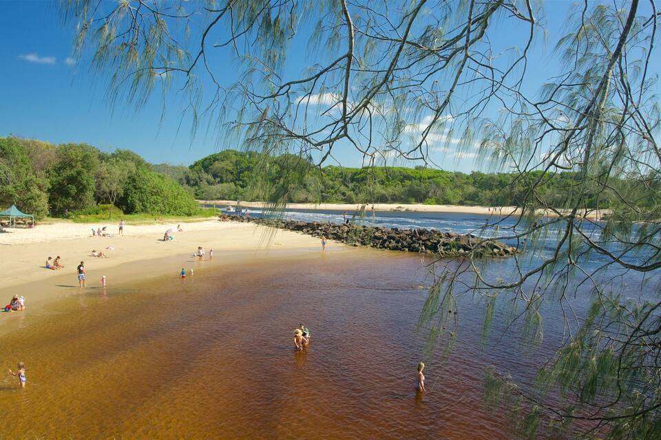 Uma praia com águas cristalinas, pessoas nadando e uma tenda ao fundo.