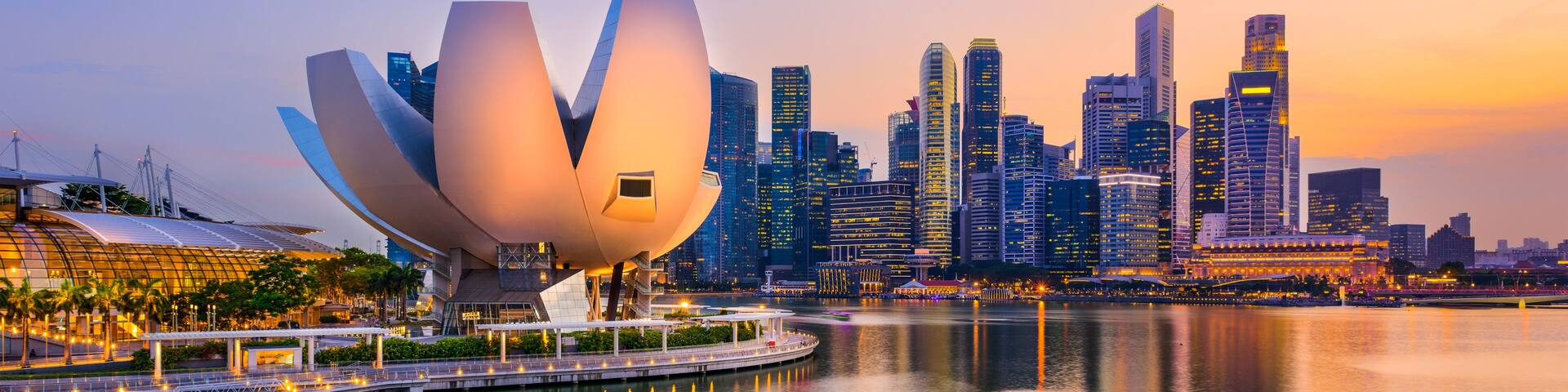 A modern architectural structure with a lotus-like design, a waterfront promenade, and a city skyline with high-rise buildings.