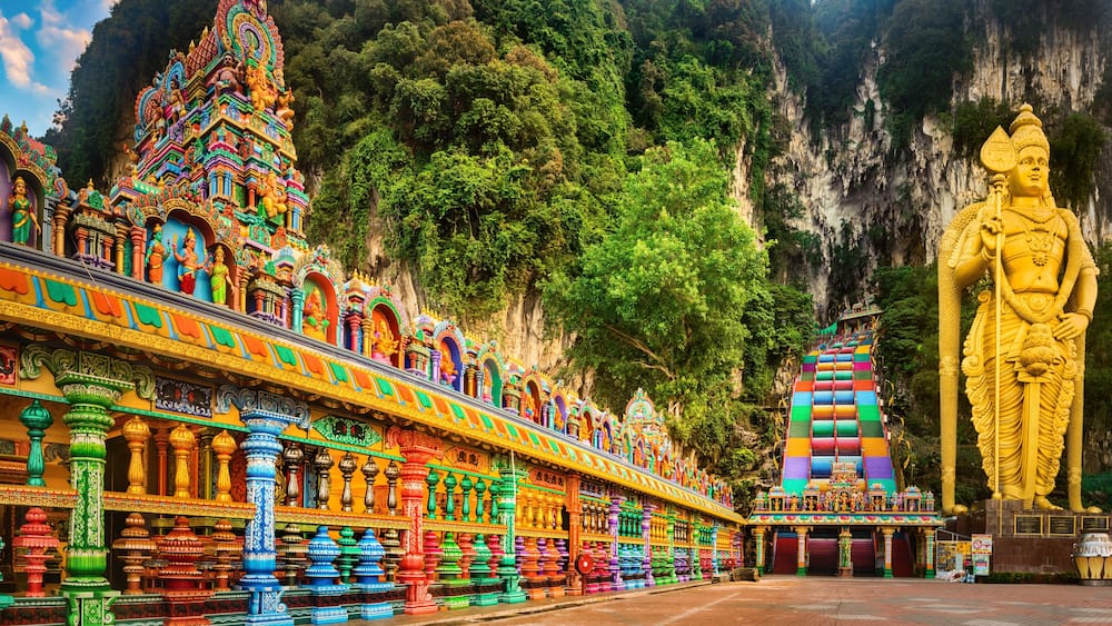 A colorful temple with intricate architecture, a large golden statue, and a mountainous backdrop.