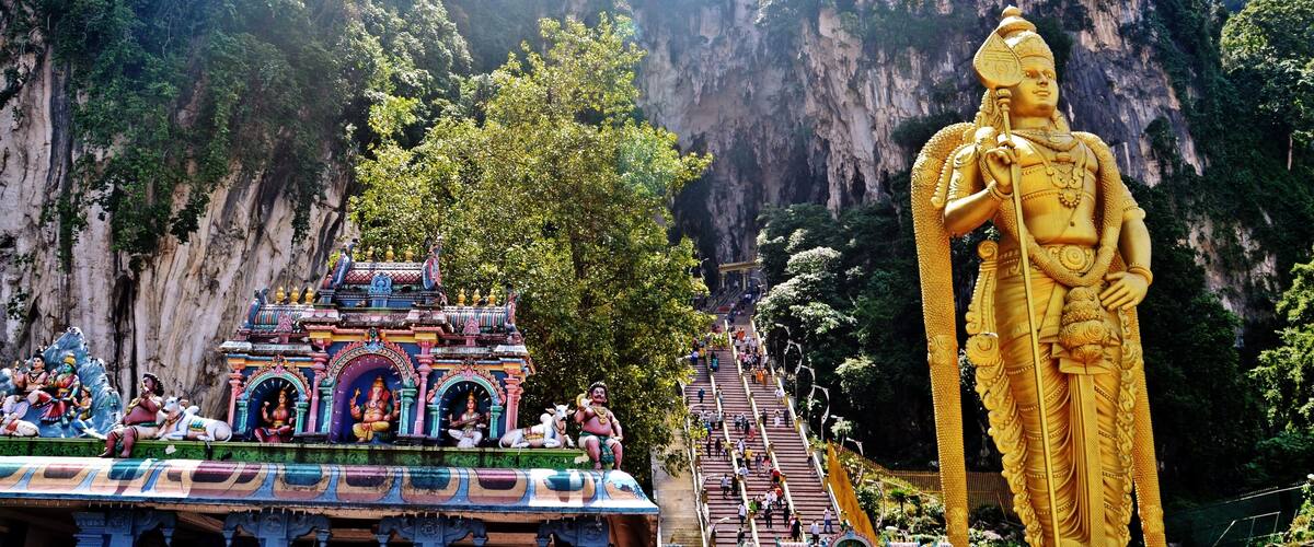 A large golden statue, a temple with colorful carvings, and a steep staircase leading up to it.