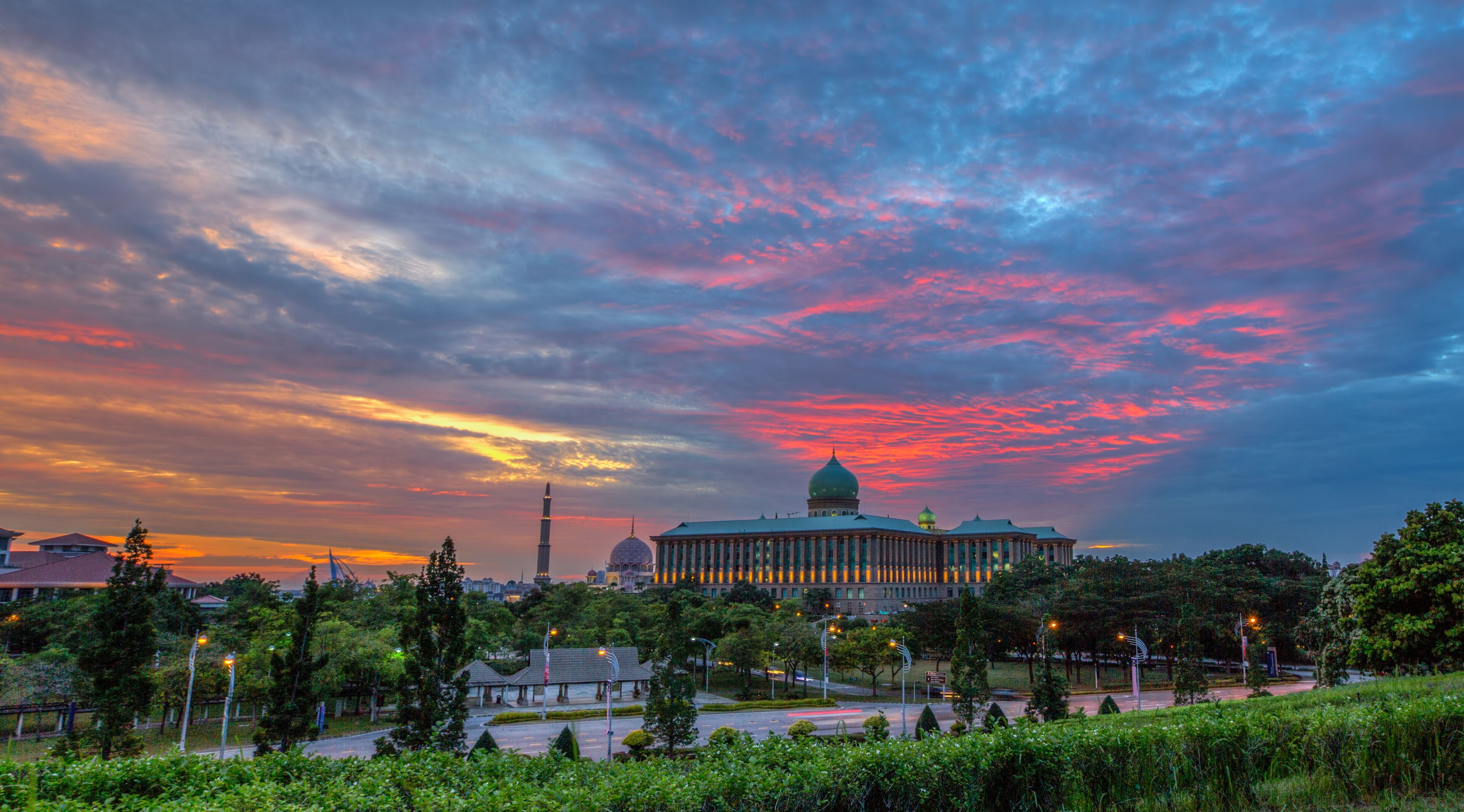 A cityscape with a prominent building featuring a dome, surrounded by greenery and a colorful sky.