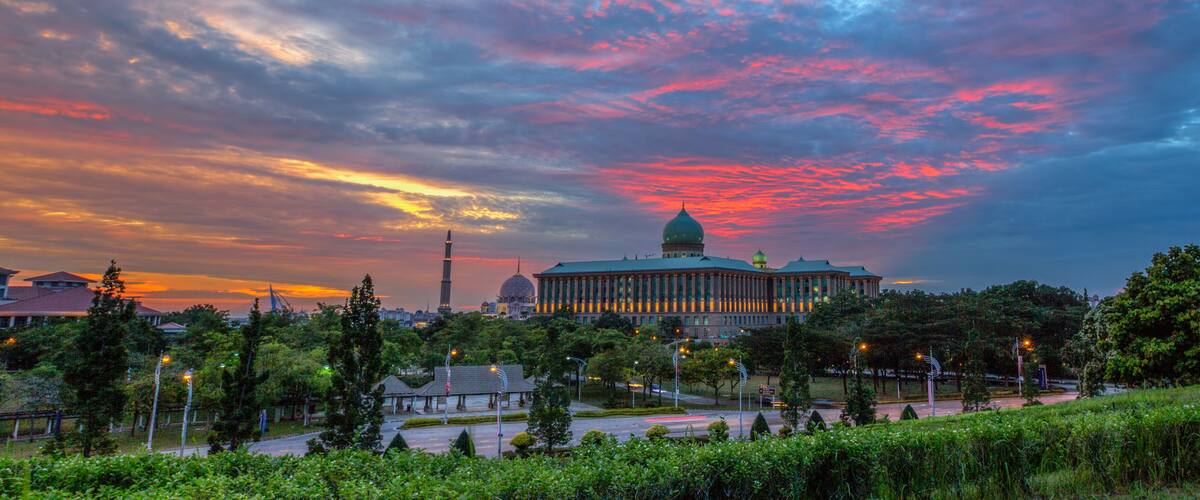 A cityscape with a prominent building featuring a dome, surrounded by greenery and a colorful sky.