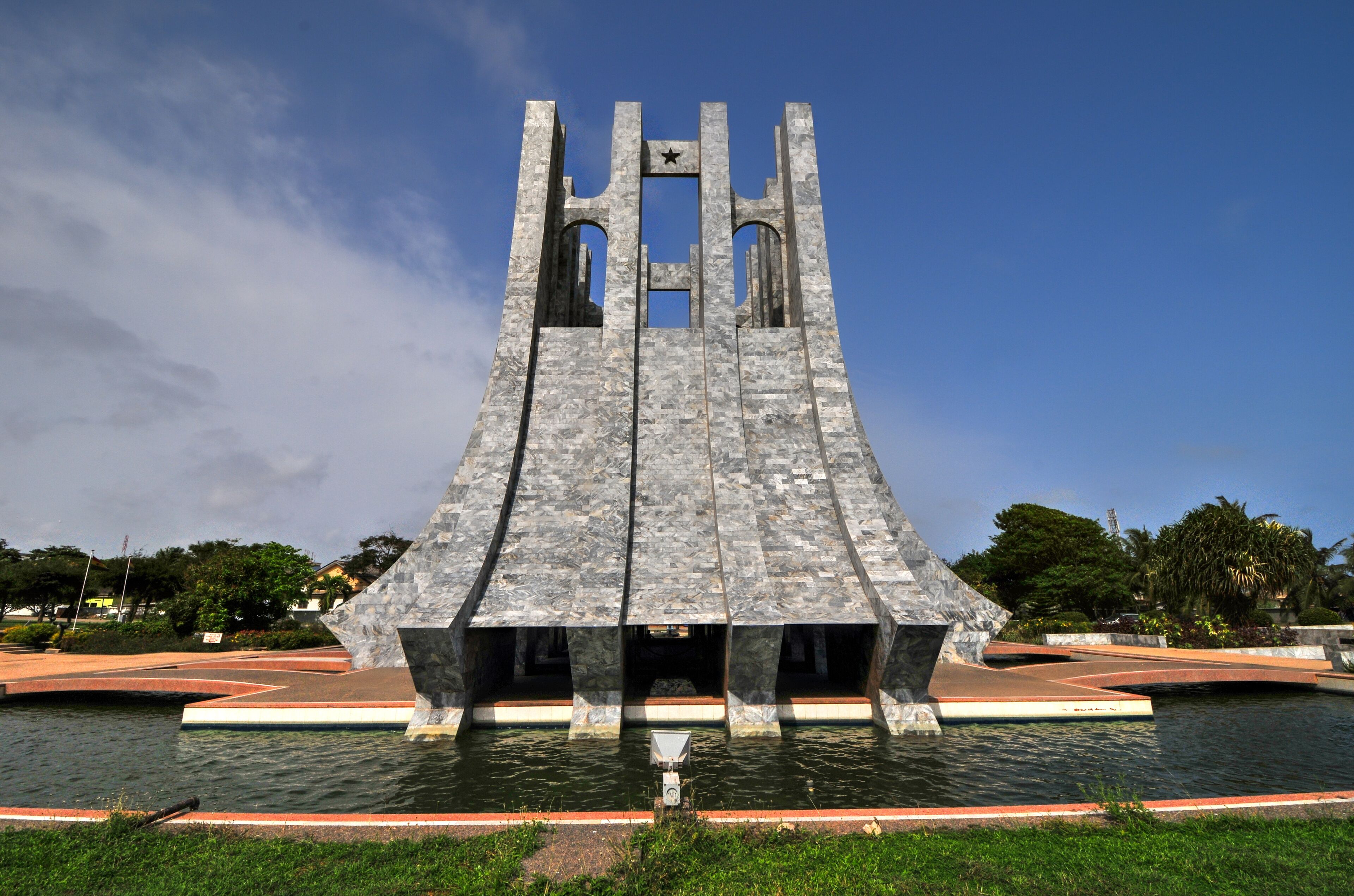 A large, modern sculpture with a star on top, situated in a park with a body of water in front.