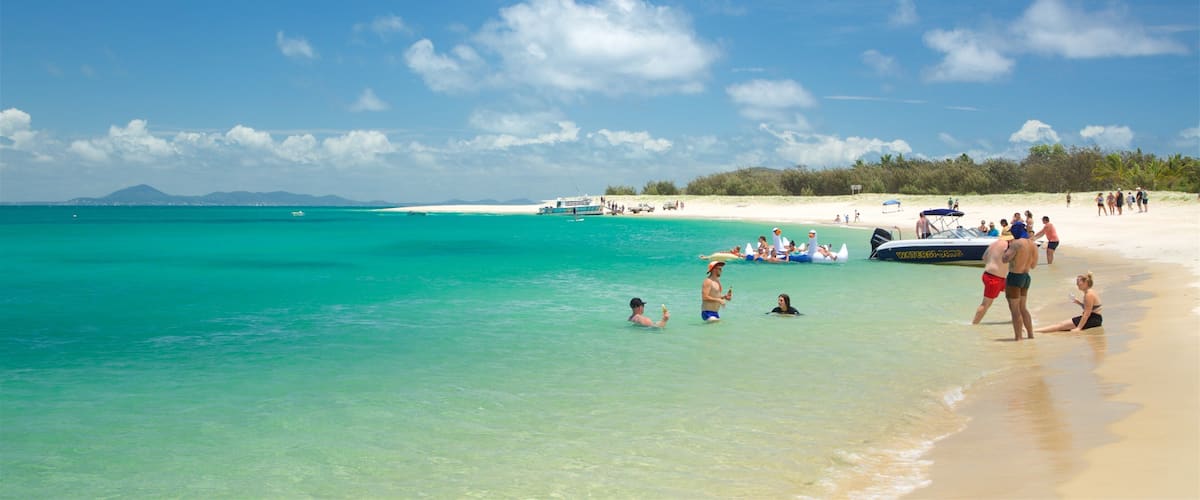 A beach with clear turquoise water, people swimming and sunbathing, and a boat in the distance.