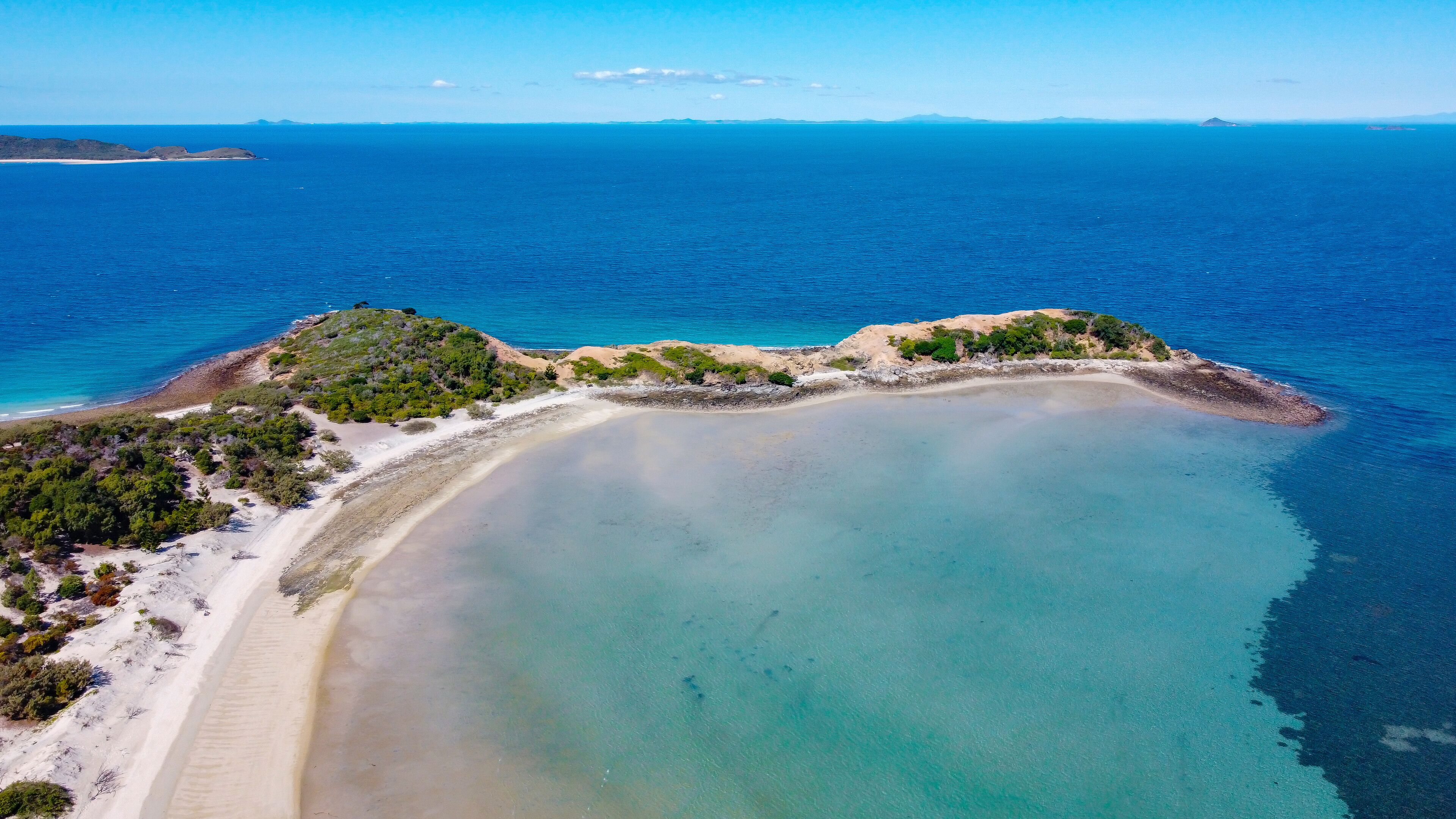 Vista aérea de un paisaje costero con una playa arenosa, una pequeña isla con vegetación y un mar azul cristalino.