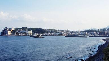 A coastal cityscape with buildings, a lighthouse, and a rocky shoreline.