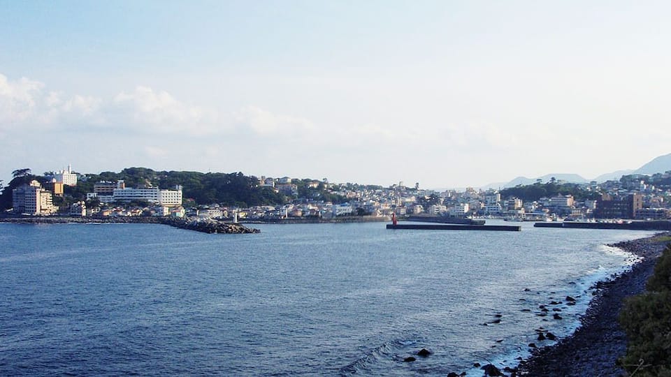 A coastal cityscape with buildings, a lighthouse, and a rocky shoreline.