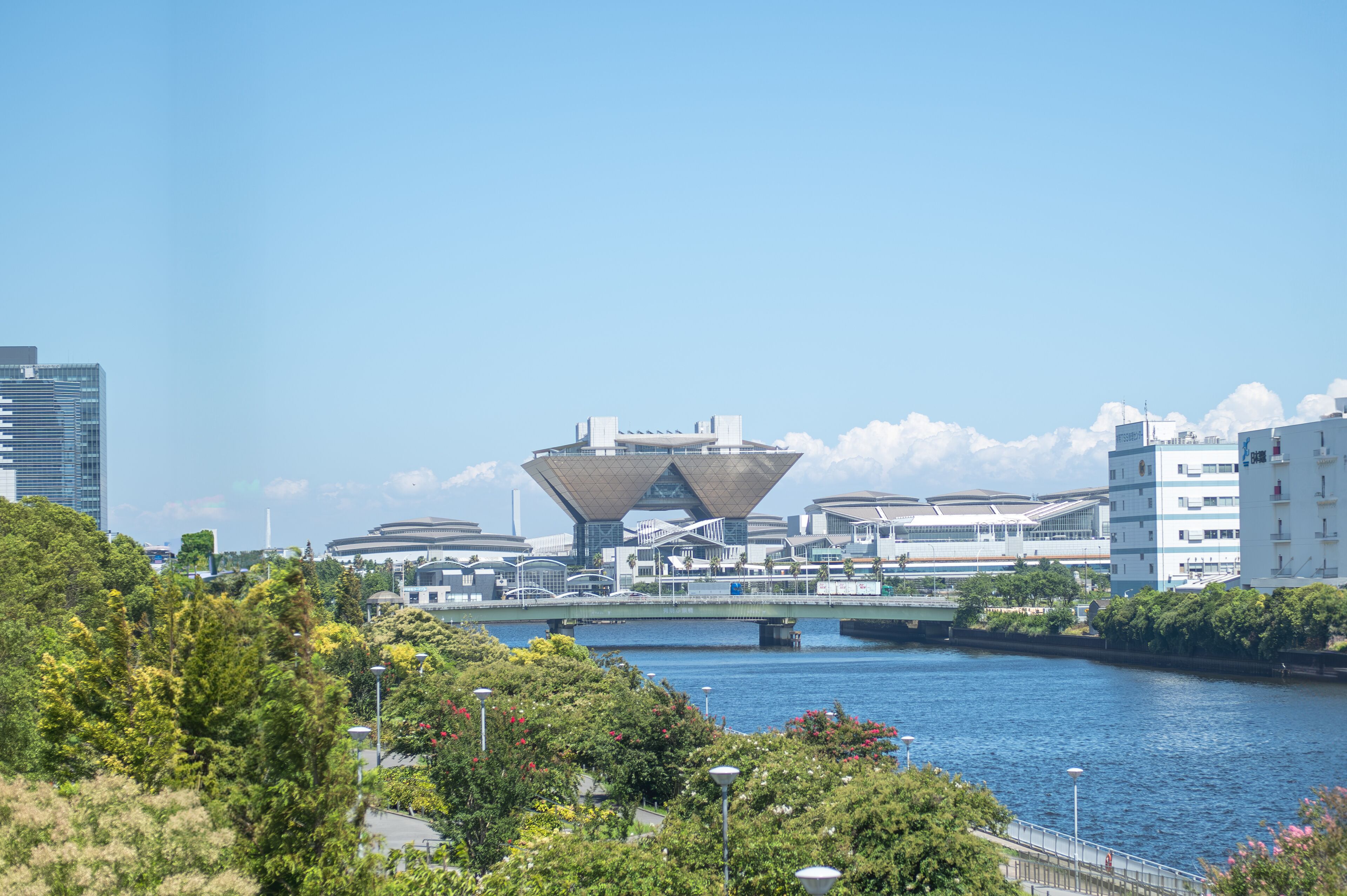 Uma estrutura arquitetônica moderna junto a um rio, cercada por vegetação e edifícios urbanos.