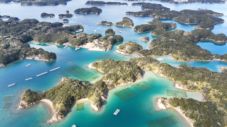 An aerial view of a coastal area with numerous small islands, clear blue waters, and several boats.