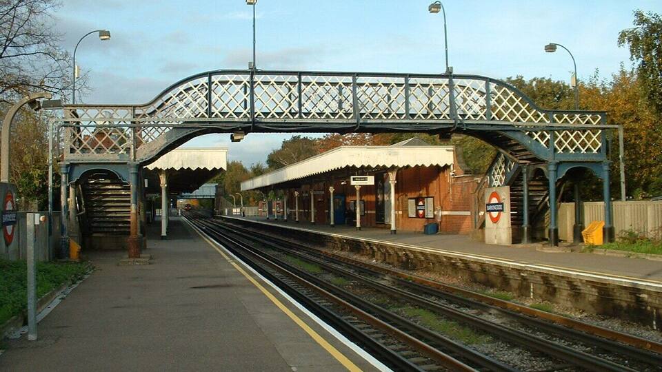 A railway station with a covered platform, a bridge overhead, and multiple tracks.