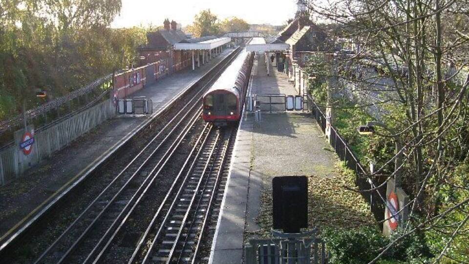 A train station with multiple tracks, a platform, and a bridge in the background.