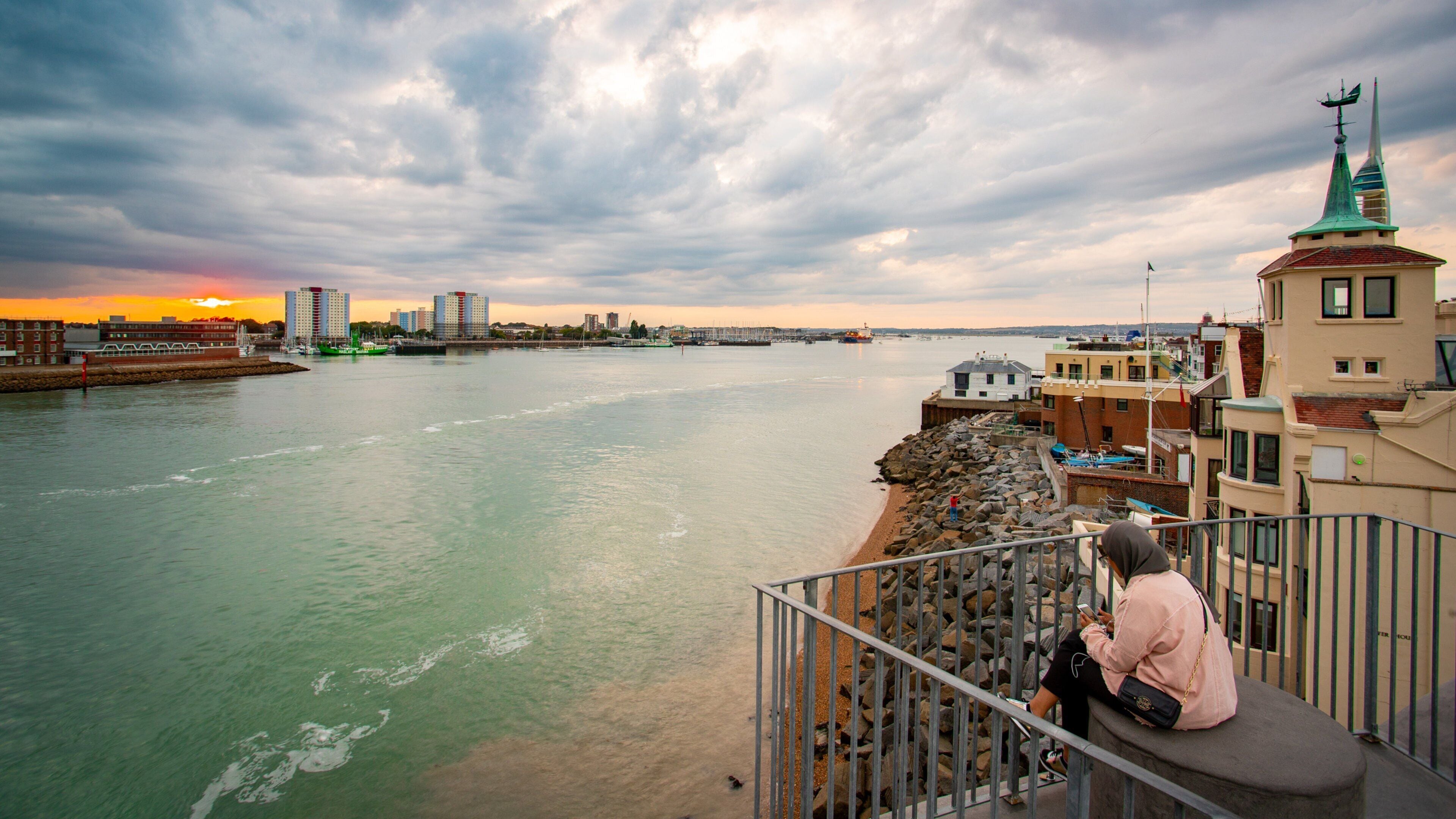 A waterfront cityscape with a river, buildings, and a sunset.