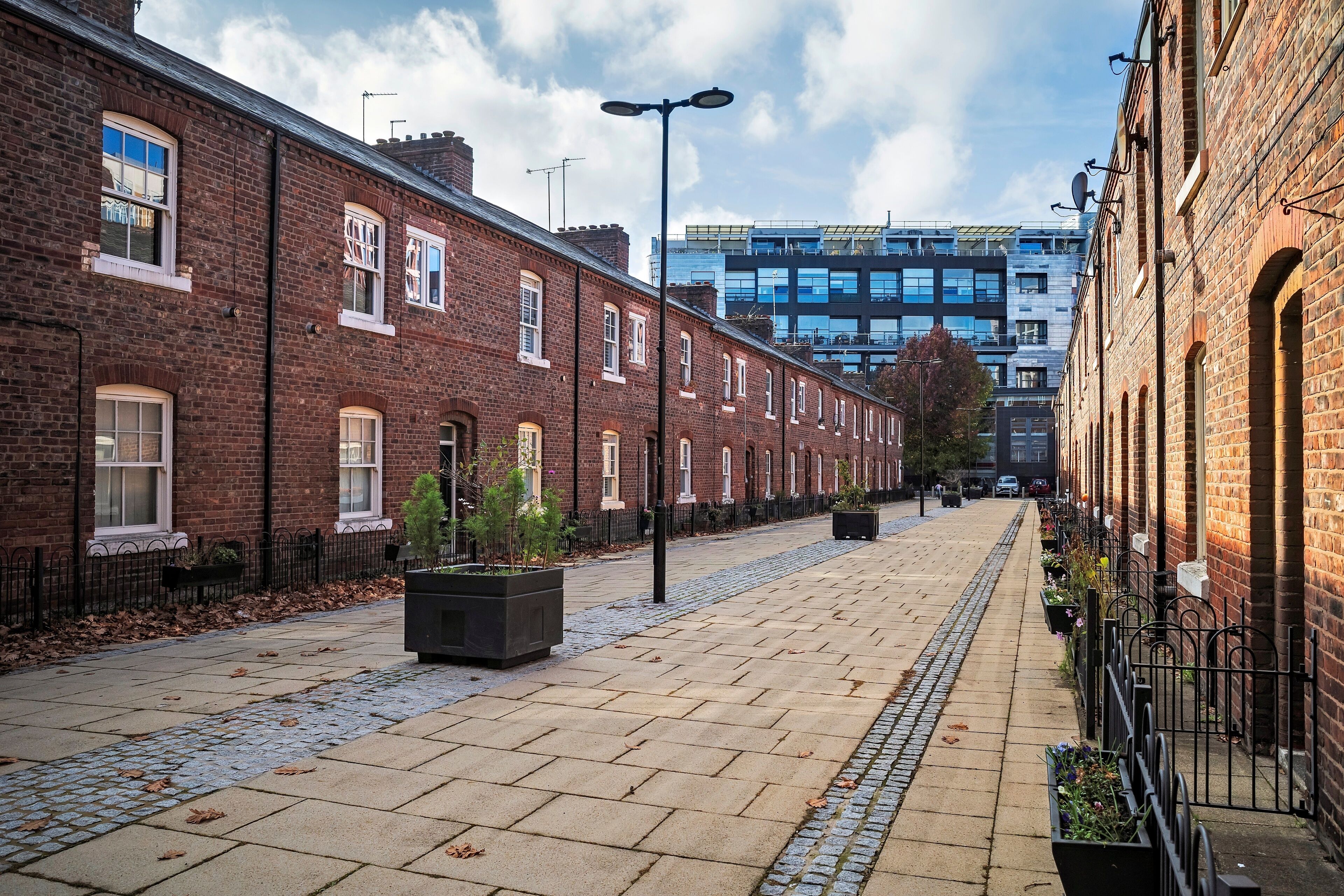 A brick-lined street with a cobblestone path, a modern building in the background, and a clear sky.