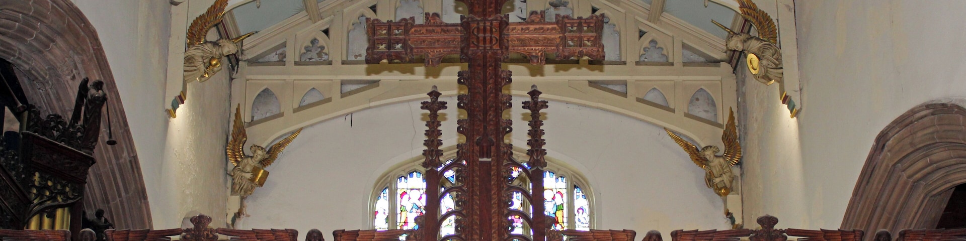 Eine kunstvoll gestaltete Holztubu mit Glasfenstern und Engelsstatuen in einer Kirche.