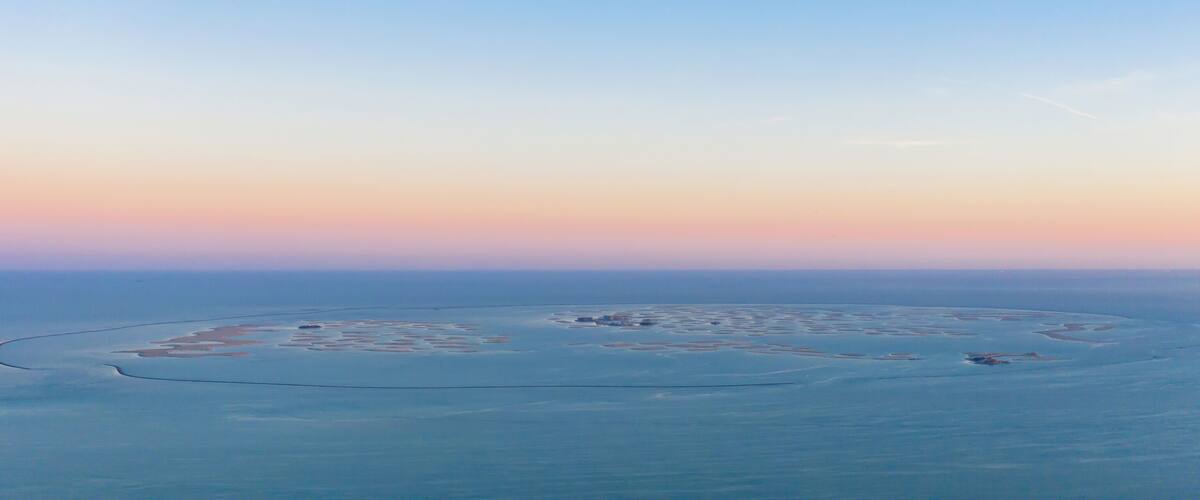 An aerial view of a large salt flat with a circular pattern of smaller mounds and a curved line of water.