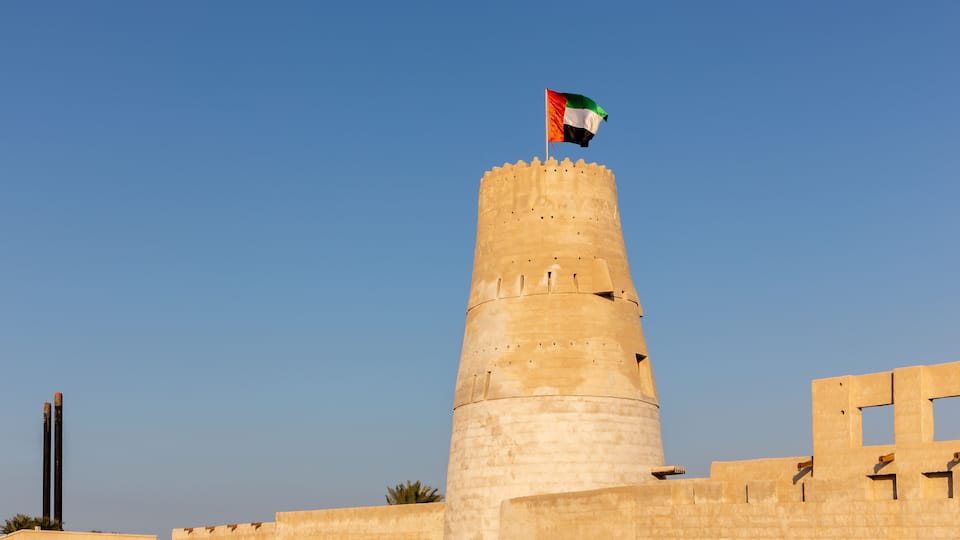 Stone arabic watchtower with waving United Arab Emirates National Flag in Al Jazirah Al Hamra haunted town in Ras Al Khaimah.