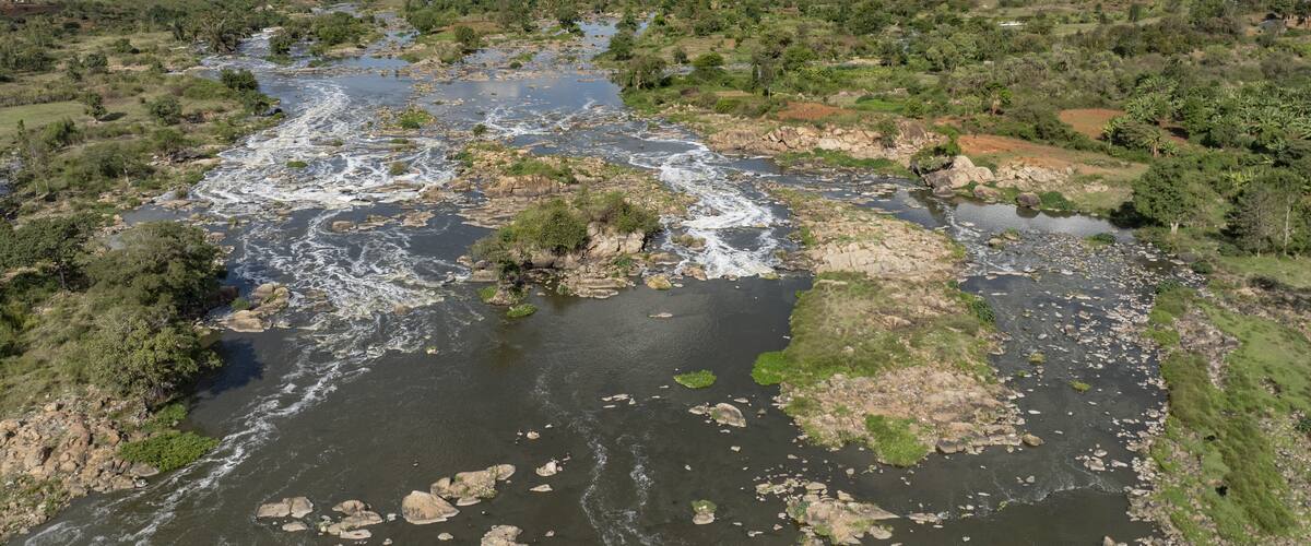 Aerial view of the rushing river cascading over rugged rocks, framed by vibrant greenery under a vast sky, Kilimambogo, Kiambu County, Kenya.