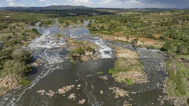 Aerial view of the rushing river cascading over rugged rocks, framed by vibrant greenery under a vast sky, Kilimambogo, Kiambu County, Kenya.