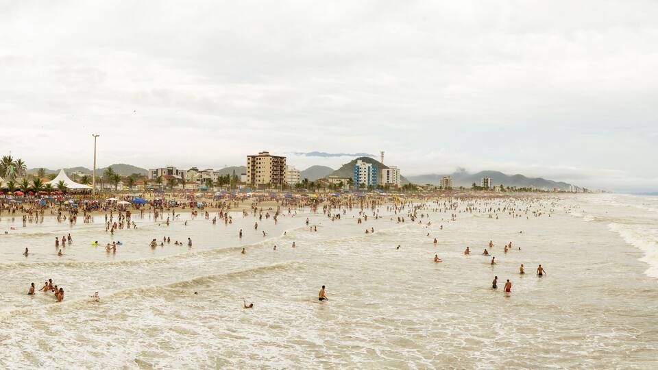 A crowded beach with people swimming and walking along the shore.