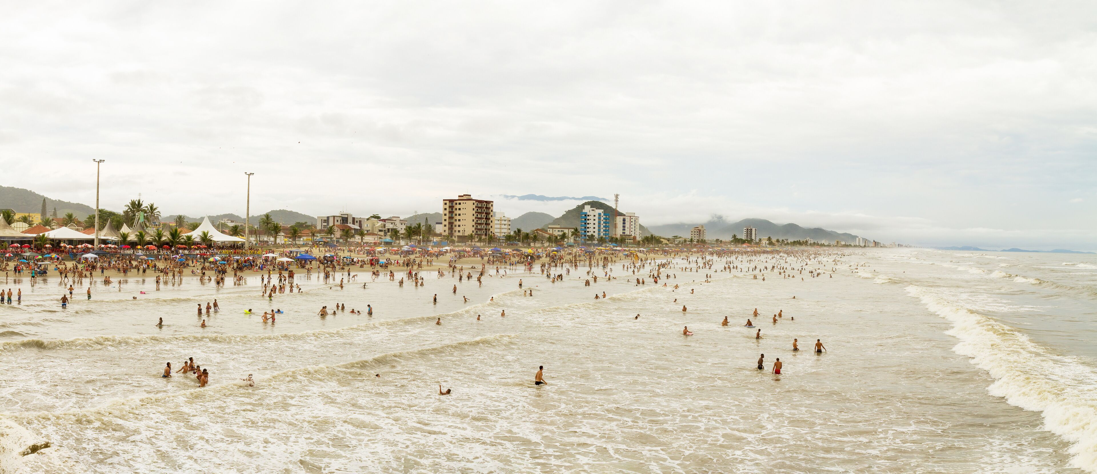 A crowded beach with people swimming and walking along the shore.