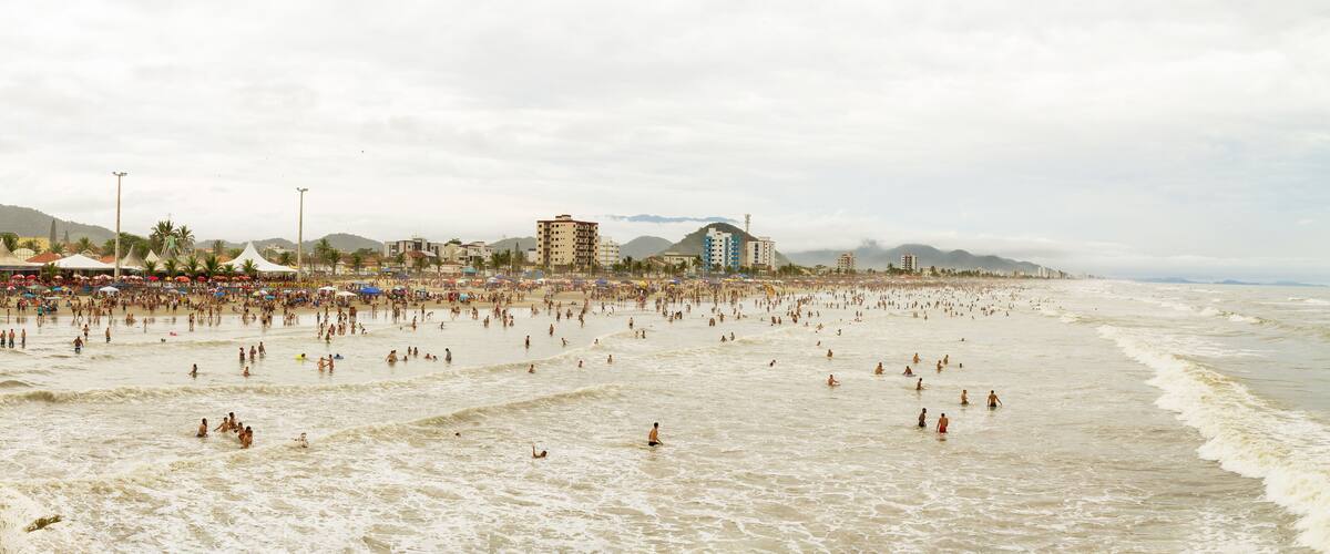 A crowded beach with people swimming and walking along the shore.