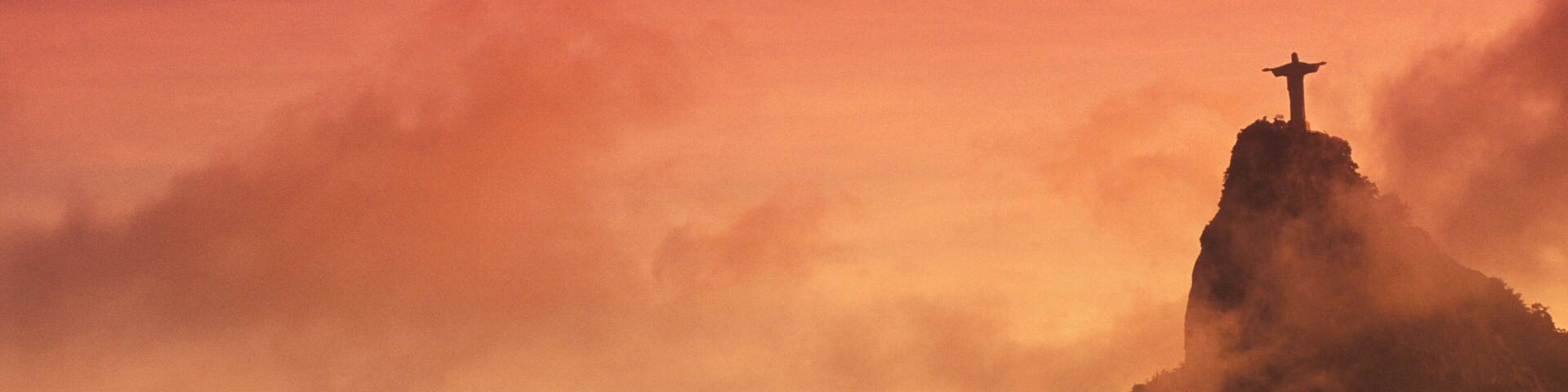 A mountain peak with a cross at the summit, surrounded by clouds.