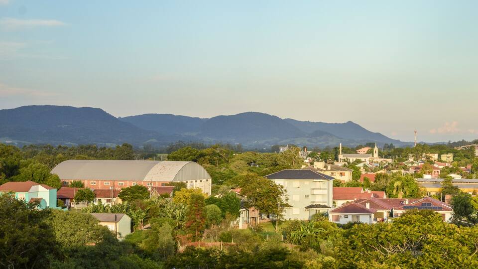A town with a large green building, surrounded by houses and lush greenery, with mountains in the background.