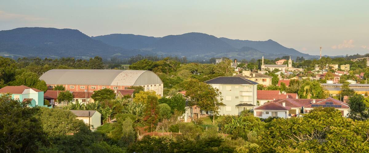 A town with a large green building, surrounded by houses and lush greenery, with mountains in the background.