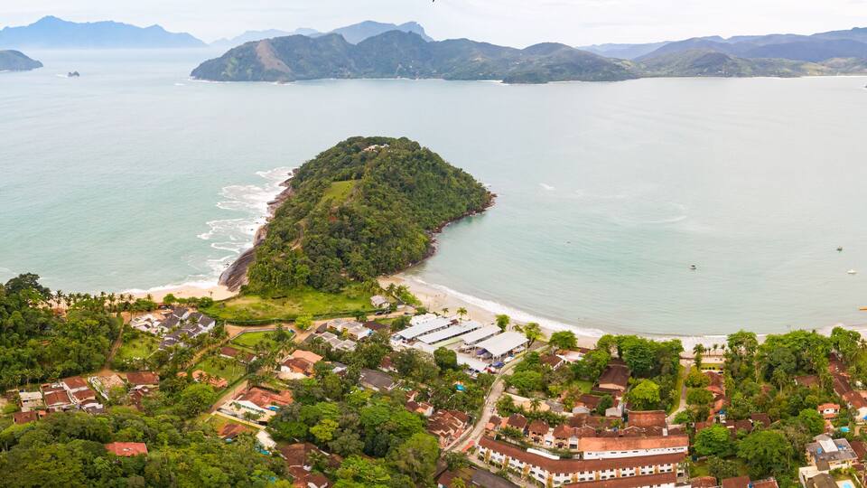 Un pueblo costero con una playa, rodeado de exuberante vegetación y montañas.