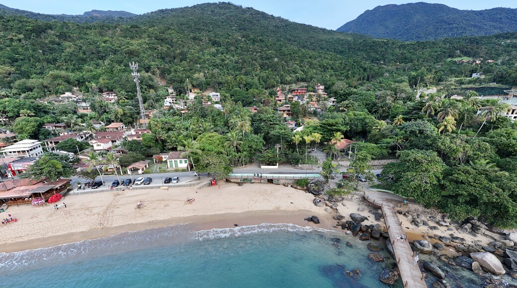 Visão aérea do píer na Praia Grande em Ilhabela, SP, com mar azul, faixa de areia e estrutura de madeira sobre a água, em cenário litorâneo tropical