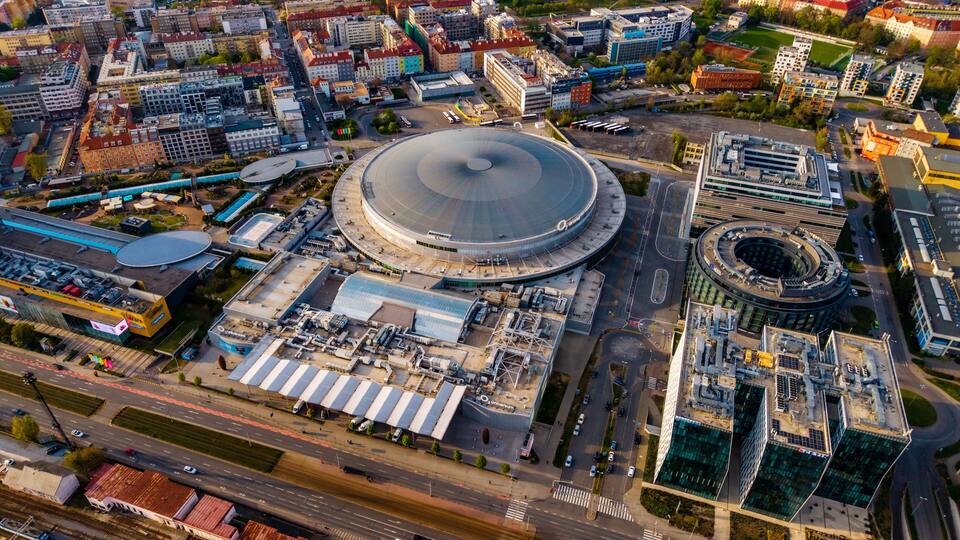 Cheskomoravska, Czechia - 21 April 2026: Aerial view of O2 arena surrounded by modern office buildings and residential blocks under clear sunlight.