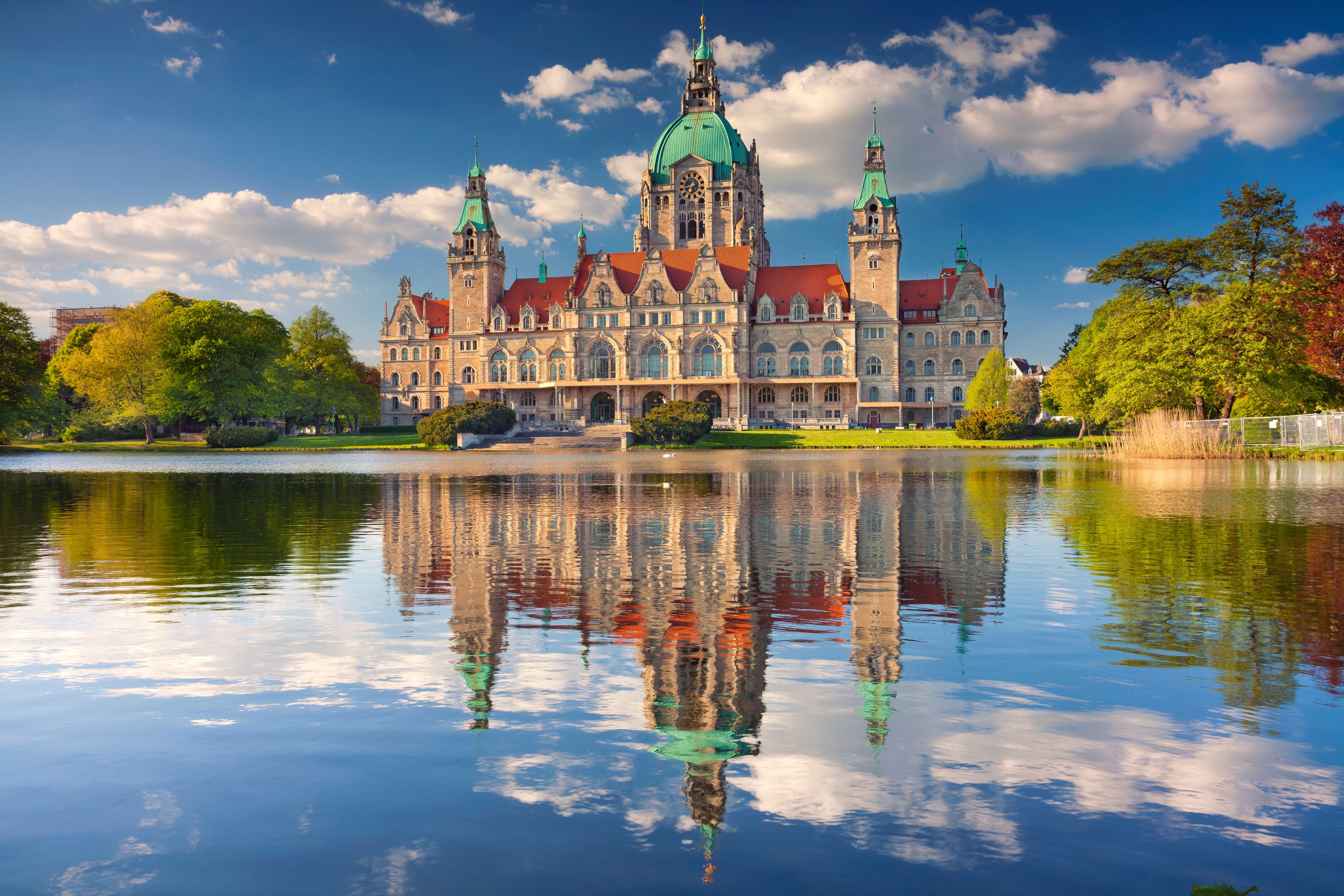 A historic building with multiple towers and a large clock, reflecting in a calm body of water.