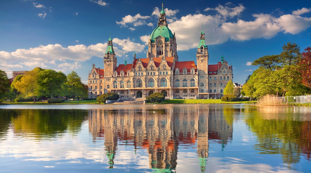 A historic building with multiple towers and a large clock, reflecting in a calm body of water.