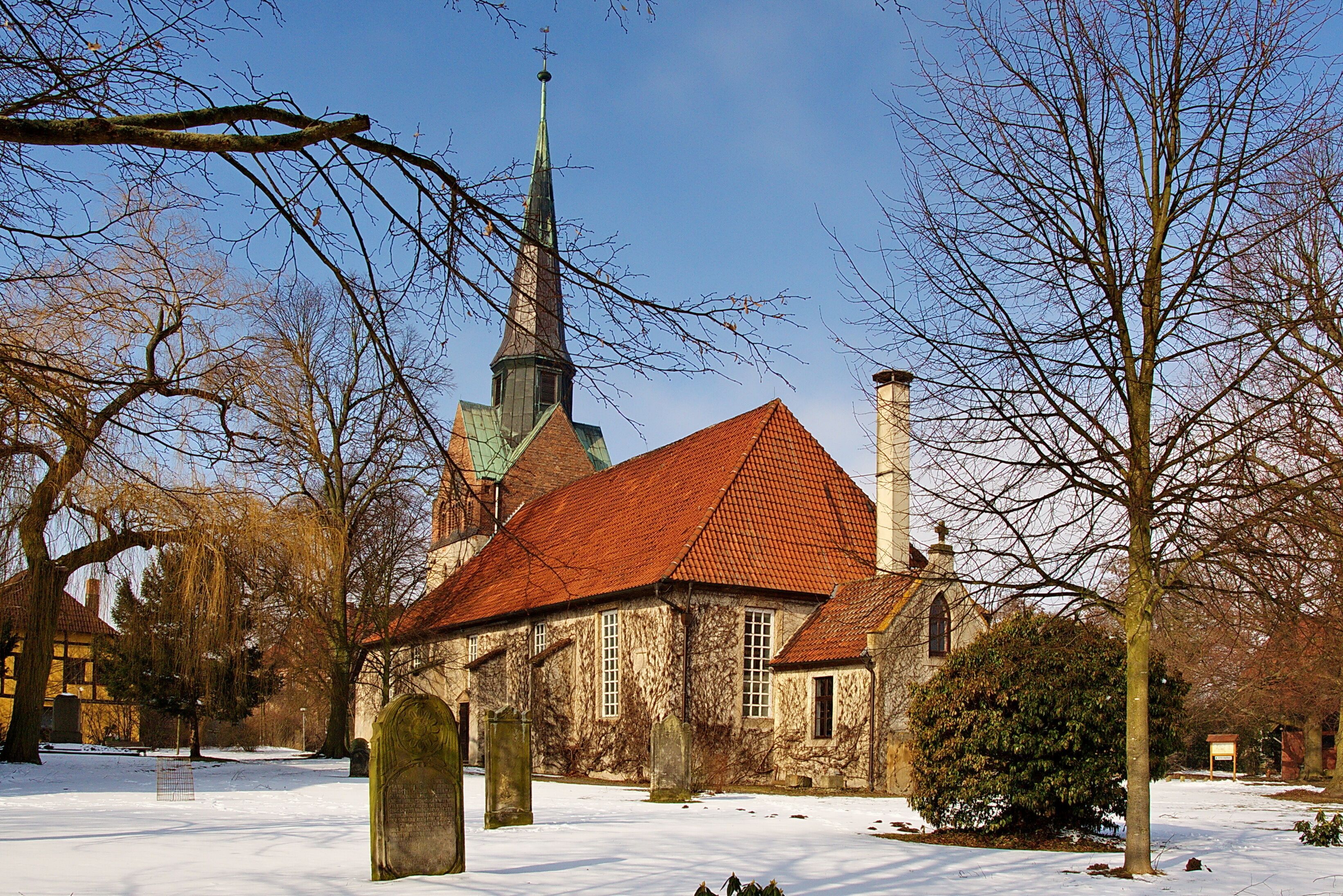 A church with a red roof and a tall steeple, surrounded by bare trees and snow.